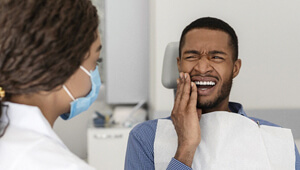 man in dental chair holding his cheek in pain