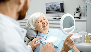 Smiling woman looking at dental implants in Odessa in mirror