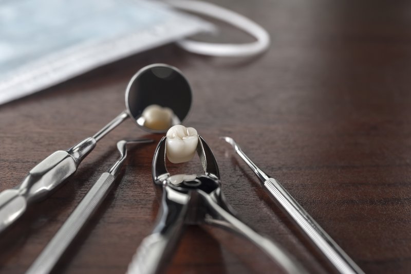 multiple dental tools lying on a table, one of which is holding an extracted tooth