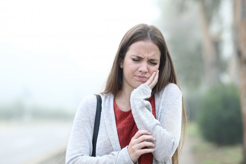 a young woman walking outside and holding her cheek due to a toothache